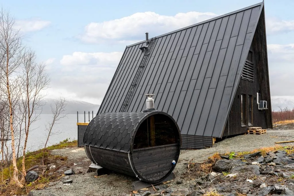 Completed black A-frame cabin with a barrel sauna on a northern shoreline, built by TUUYA
