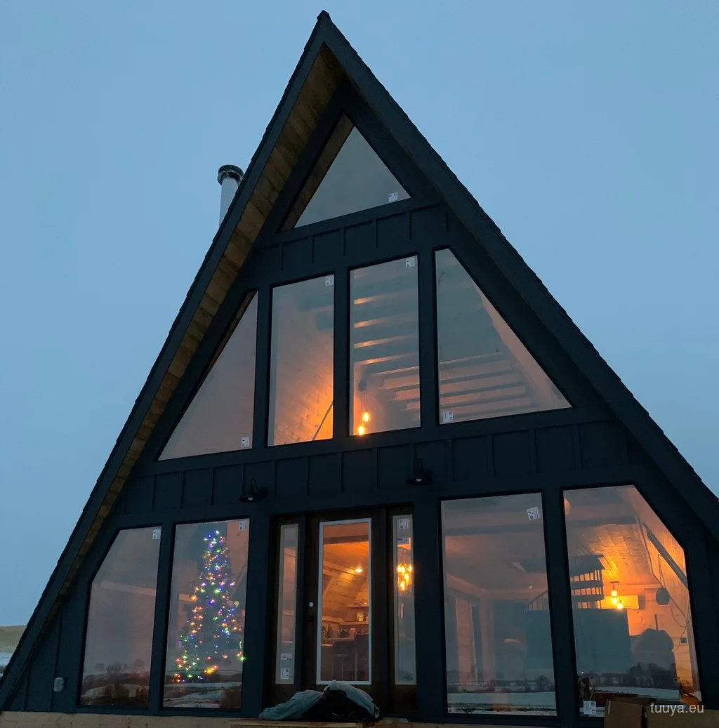 Completed A-frame cabin glowing at dusk behind full-height glazing
