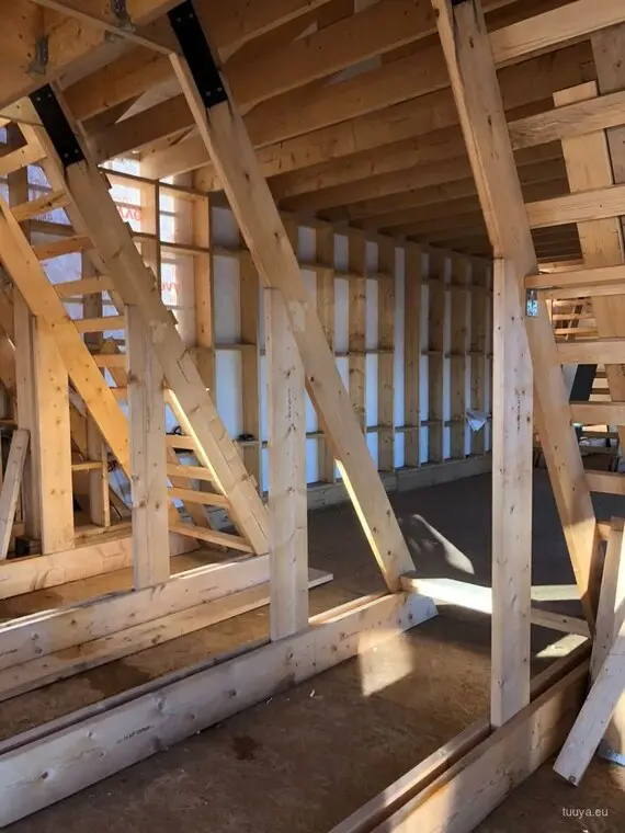 Inside an A-frame under construction: rafters landing on the floor platform, with steel connectors at the joints.