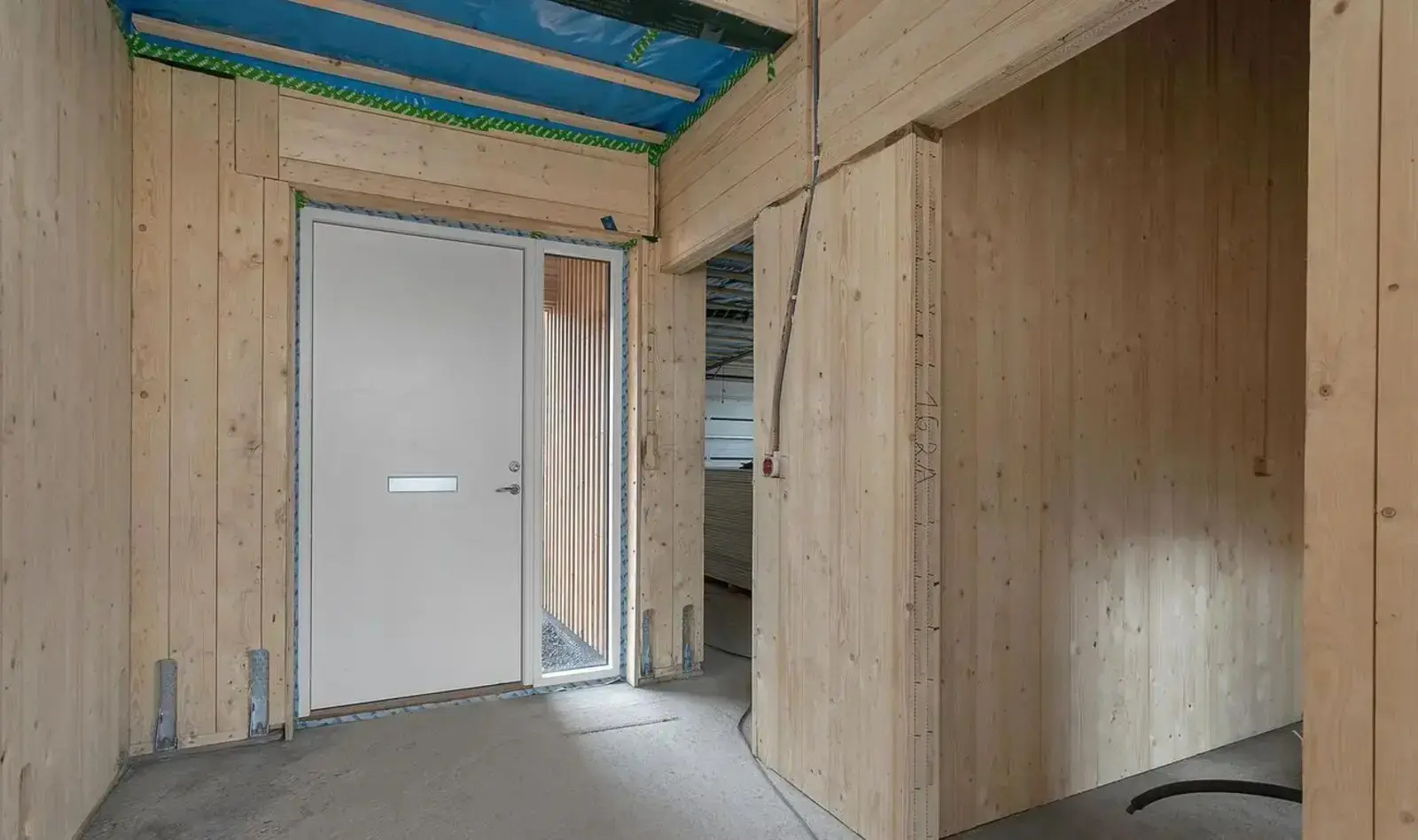 Nepabeigta telpa ar atklātām pārseguma sijām un siltumizolāciju: vissezonas moduļu mājas kvalitāte redzama šajā stadijā, ne apdares fotogrāfijās.