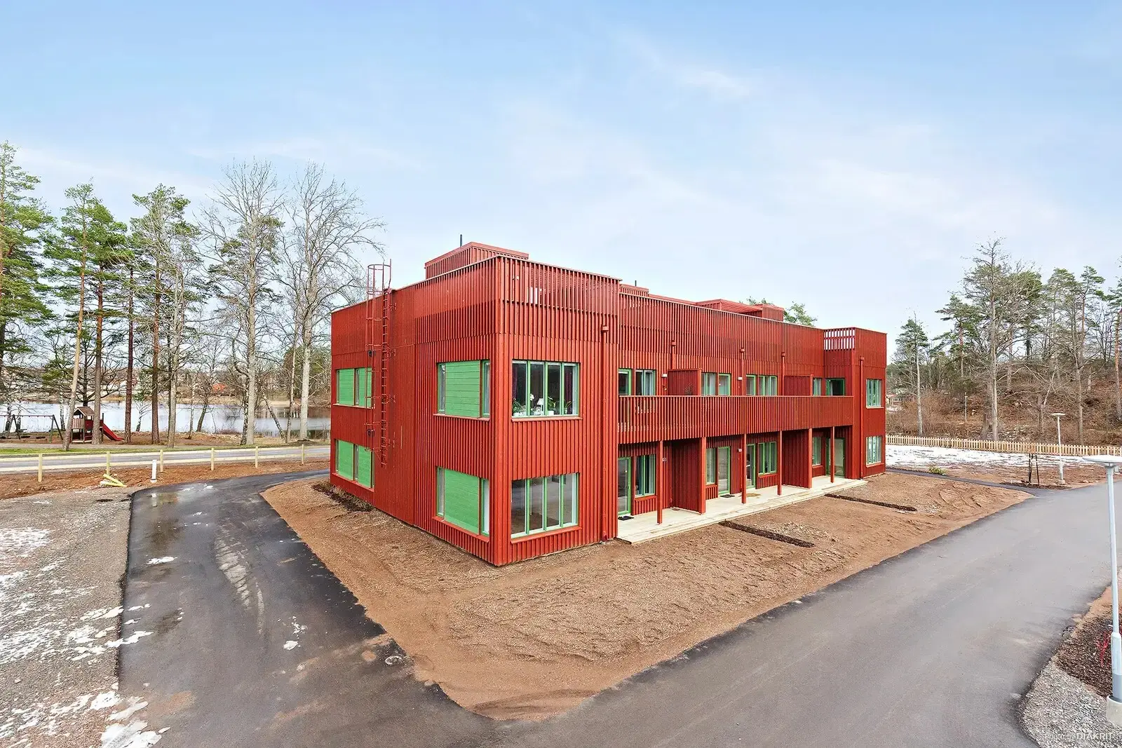 Red timber lakeside building from the access road with bare trees behind